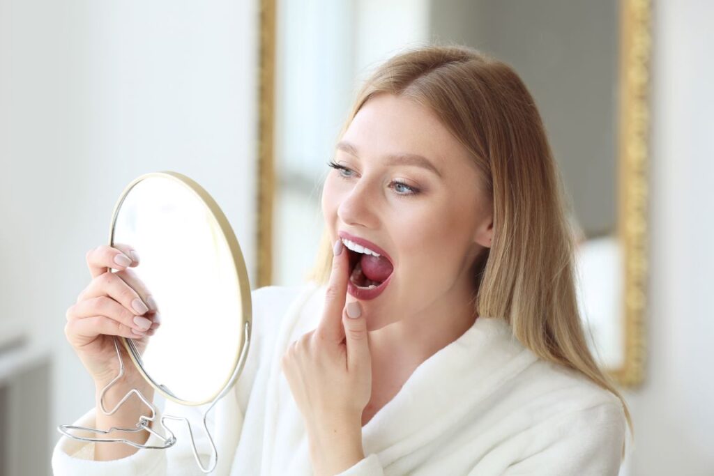 A woman looking at her teeth in a hand mirror.